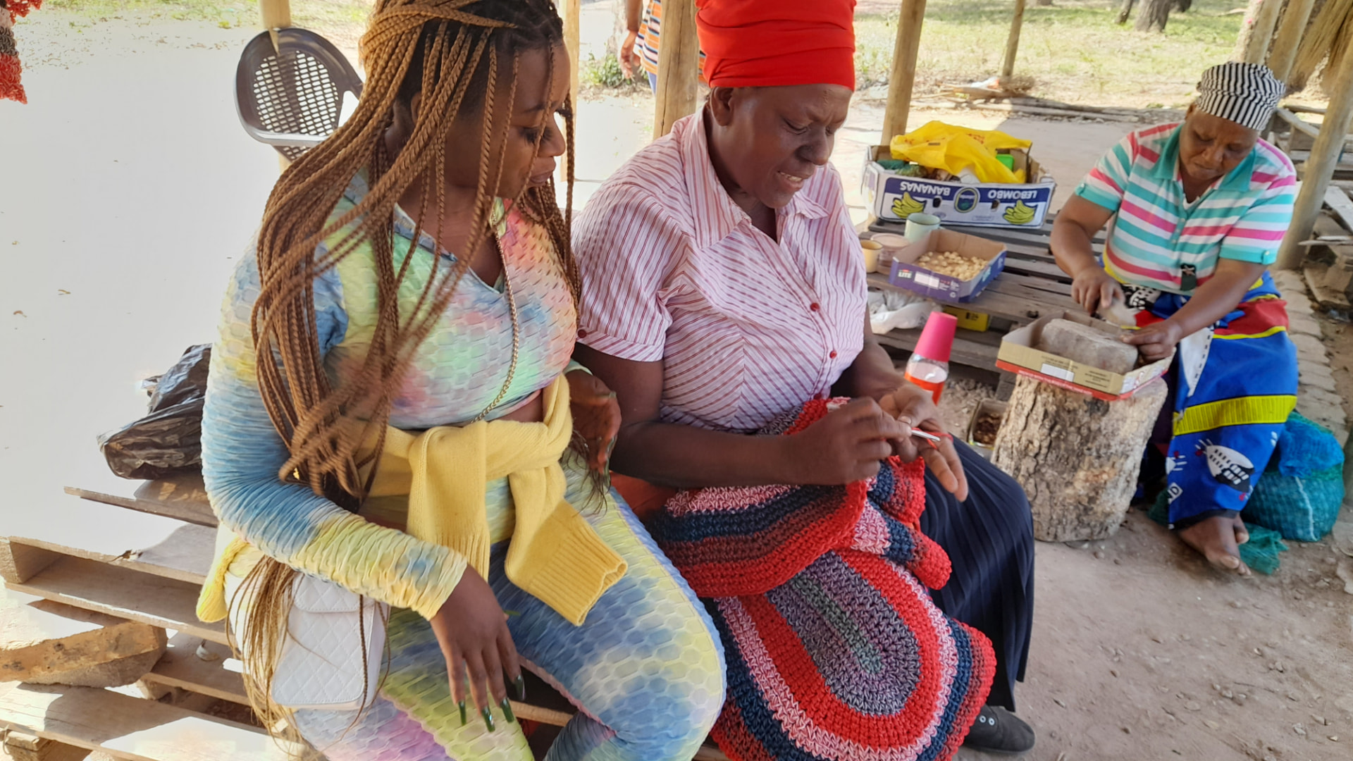 Women crocheting together under a shade structure